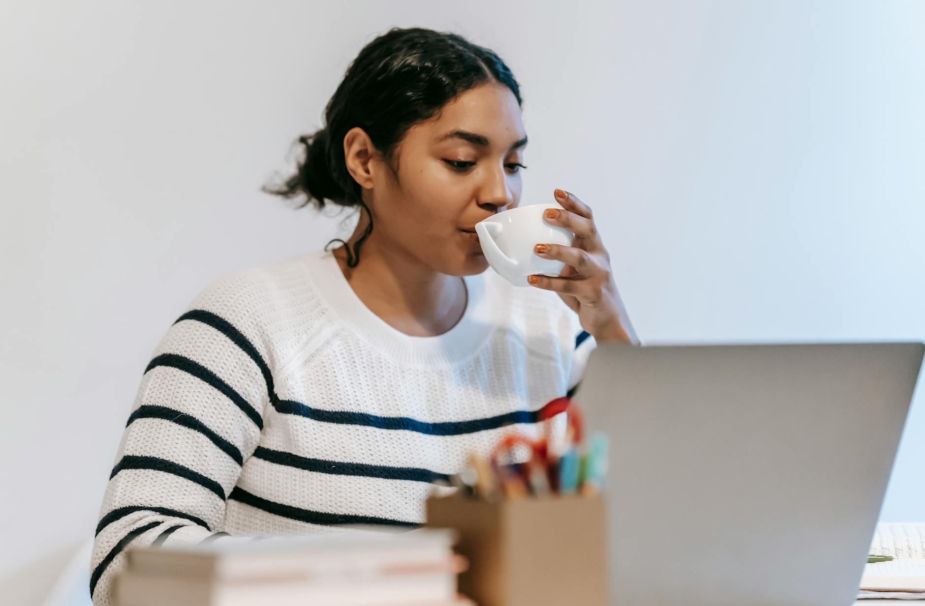 ethnic lady working remotely on laptop with cup of drink